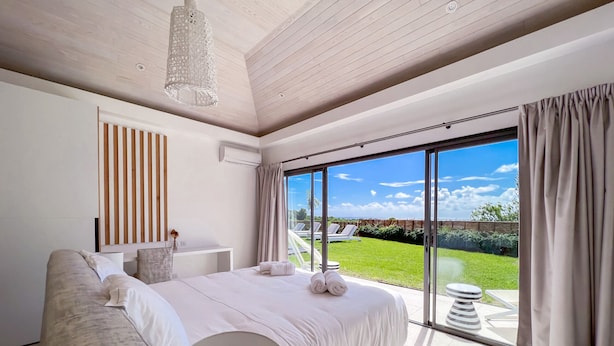 Een moderne slaapkamer met een groot bed, een nachtkastje, een hanglamp en uitzicht op een tuin door een schuifdeur.