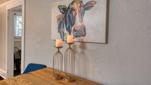 A dining area with a wooden table, two candles on candle holders, and a colorful cow painting on the wall.