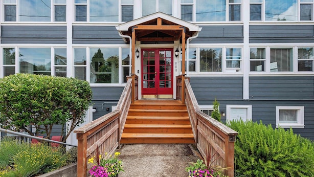Un bâtiment avec une porte rouge, un escalier en bois et un petit porche.
