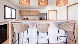 A modern kitchen with wooden cabinets, a stainless steel refrigerator, and three wicker bar stools.