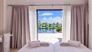 A hotel room with a large bed, two towels, and a view of a pool and palm trees.
