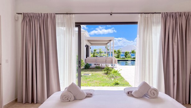 A bedroom with a large bed, two towels, and a view of a pool and outdoor seating area.