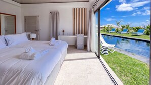 A modern hotel room with a large bed, a bathroom, and a view of a pool and garden.