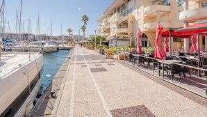 A marina with boats docked, a café area with outdoor seating, and a building with balconies. - Quartier Latin by Interhome (Fréjus)