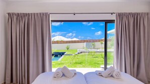 Een tweepersoonsbed met handdoeken, uitzicht op een zwembad en groen, en een heldere lucht.