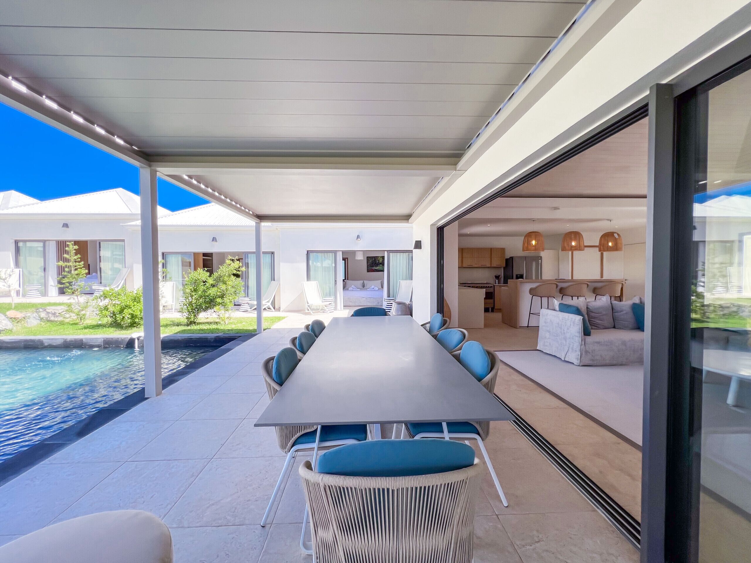 Ein moderner Essbereich im Freien mit Pool, einer überdachten Terrasse und Blick auf die angrenzenden Wohnbereiche.