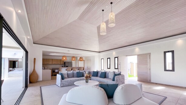 Een ruime woonkamer met een moderne bank, een rond bijzettafeltje en hanglampen.