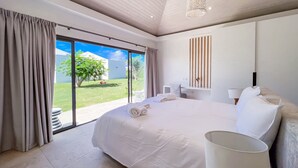 Un dormitorio moderno con una cama grande, una mesita de noche, una lámpara y vistas a un jardín a través de una puerta corredera.