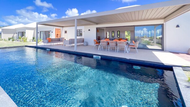 Una casa moderna con piscina, mobiliario exterior y ventanas amplias.