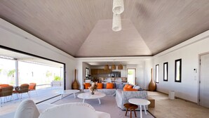 Amplia sala de estar con sofá, mesa de centro y sillones. Se observa una cocina al fondo con armarios y un refrigerador.