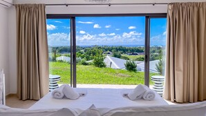 Una camera d'albergo con un letto grande, tende color beige e vista su un paesaggio verde e degli edifici.