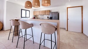 Una cucina moderna con isola centrale, tre lampade a sospensione in vimini e un'ampia finestra.