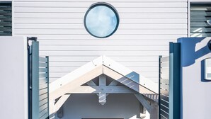 Une entrée moderne avec une fenêtre circulaire au-dessus de la porte, un toit en pente et un escalier menant à l’entrée.