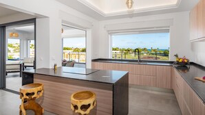 Une cuisine moderne dotée d’un grand îlot central, de tabourets en bois et offrant une vue sur l’extérieur.