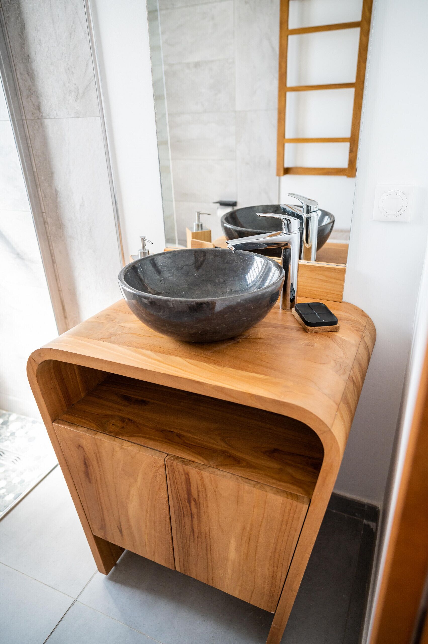 A modern bathroom with a wooden vanity, a large black bowl sink, and a mirror.