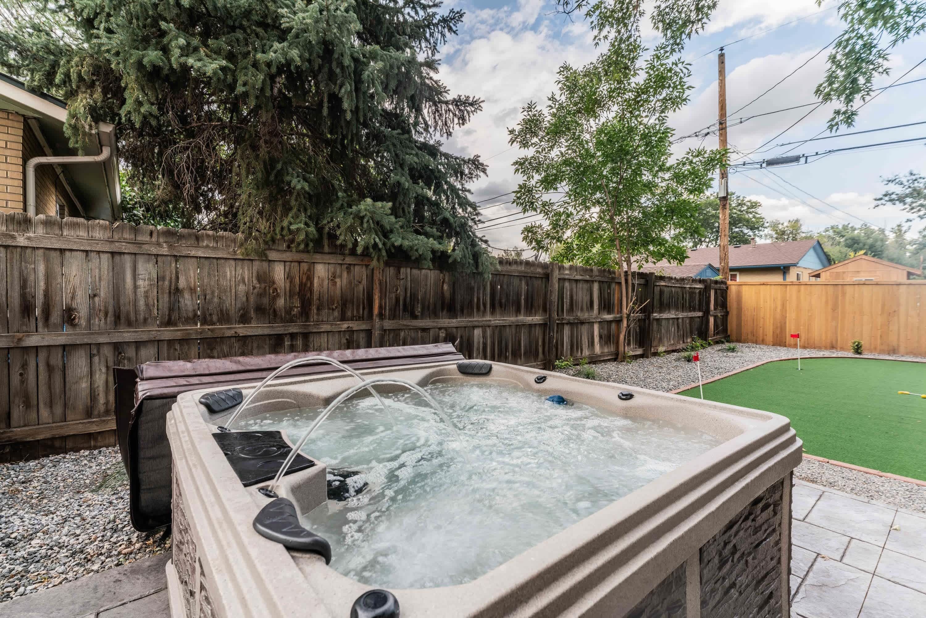 A hot tub in a backyard with a wooden fence, a lawn, and a house in the background.