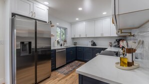 A modern kitchen with stainless steel appliances, dark blue cabinets, and a white countertop. - Game Room- Hot Tub- Sauna & Projector! (Arvada)