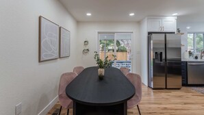 A modern kitchen with a large stainless steel refrigerator, wooden flooring, and a dining area with a black table and pink chairs. - Game Room- Hot Tub- Sauna & Projector! (Arvada)
