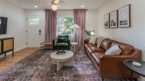 A living room with a brown leather sofa, a green velvet chair, a coffee table, and a television on a stand. - Game Room- Hot Tub- Sauna & Projector! (Arvada)
