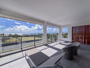 Un balcon moderne offrant une vue sur un paysage côtier, avec un espace salon comprenant une table et un paravent en bois pour plus d’intimité.