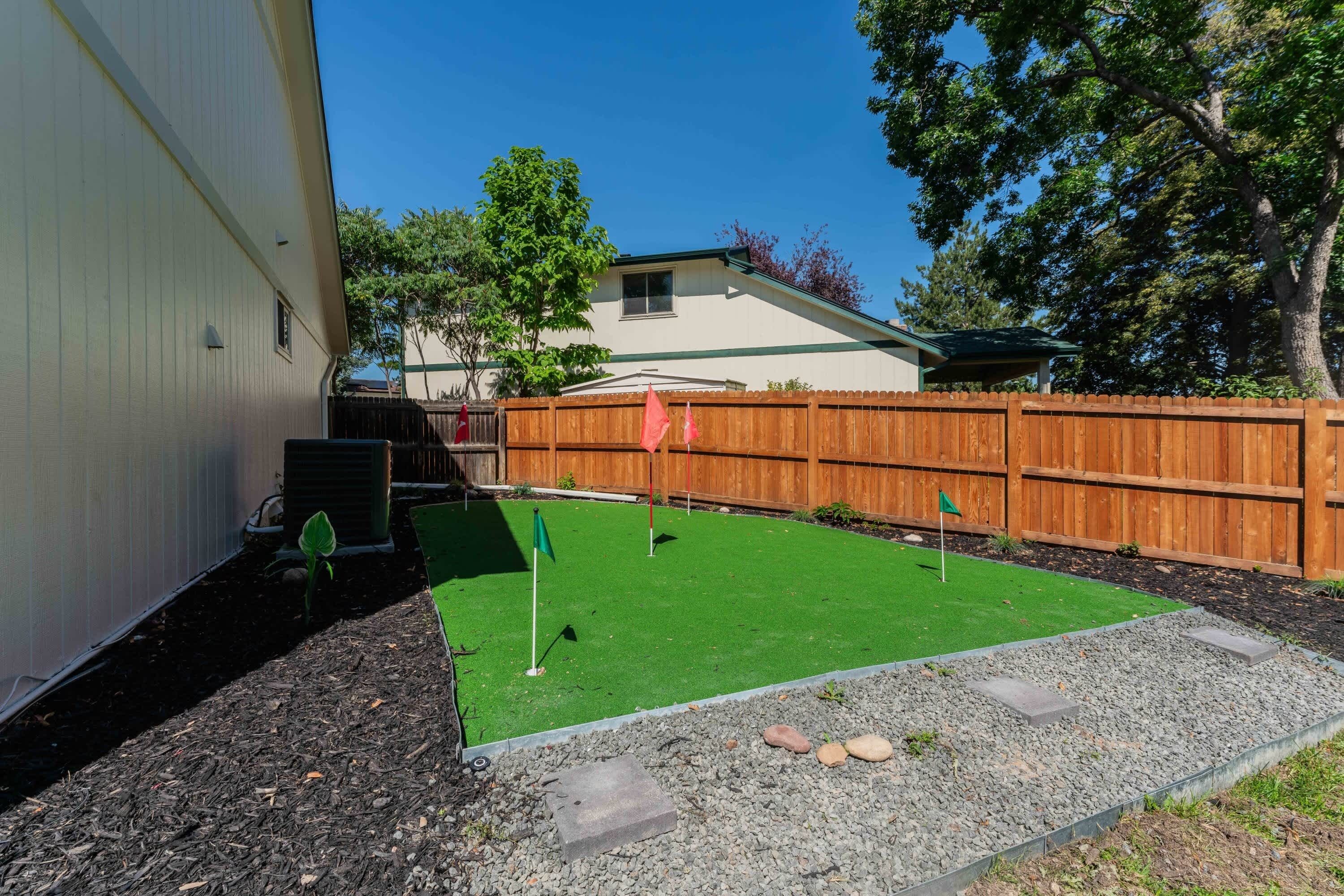 A backyard with artificial turf, a wooden fence, and a small garden area with rocks and plants.