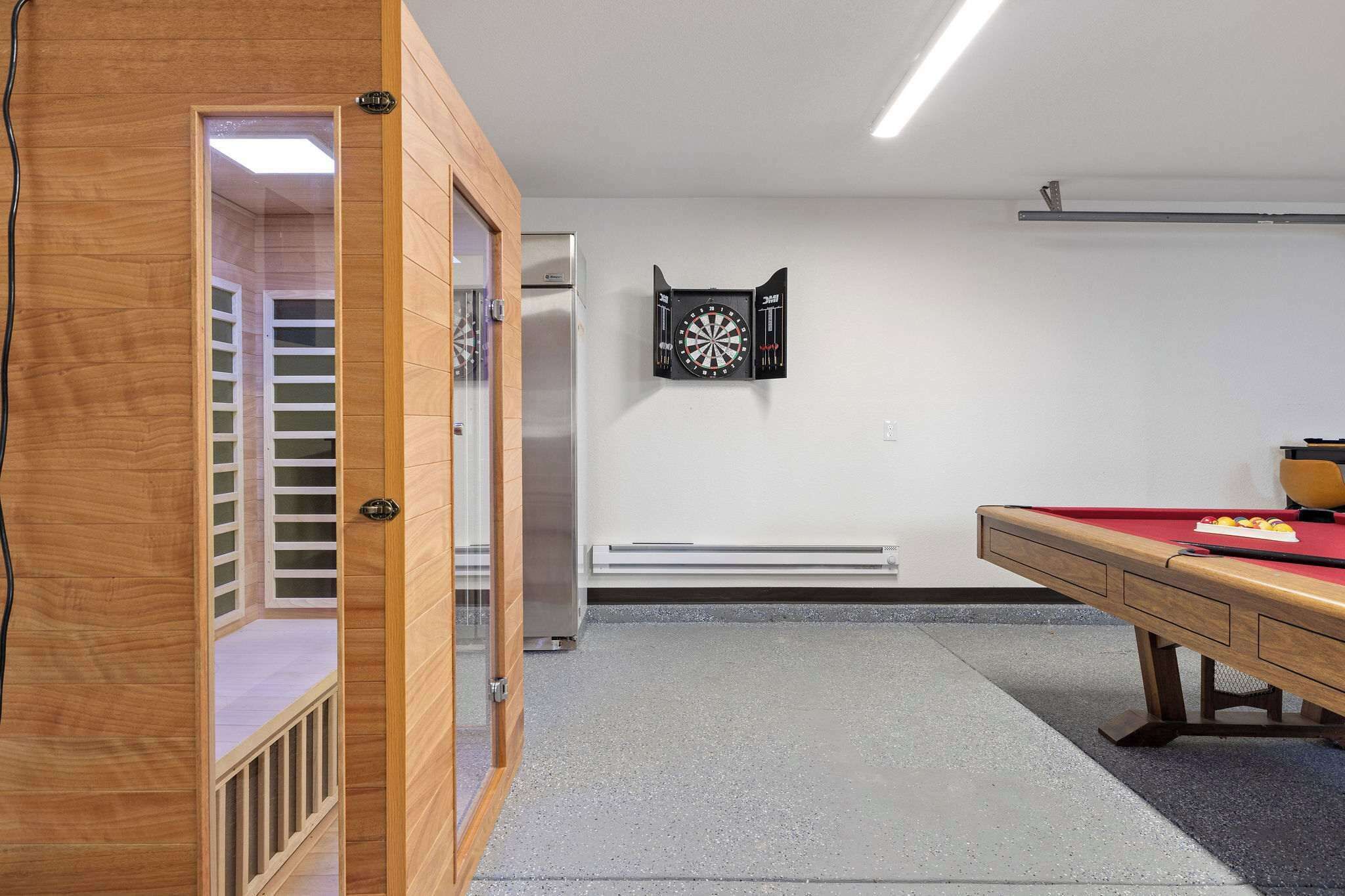 A room with a pool table, a dartboard, and a wooden door leading to a balcony.