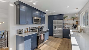A modern kitchen with dark blue cabinets, stainless steel appliances, and a large island. - Spacious home with Game Room, Hot Tub & Sauna! (Westminster)
