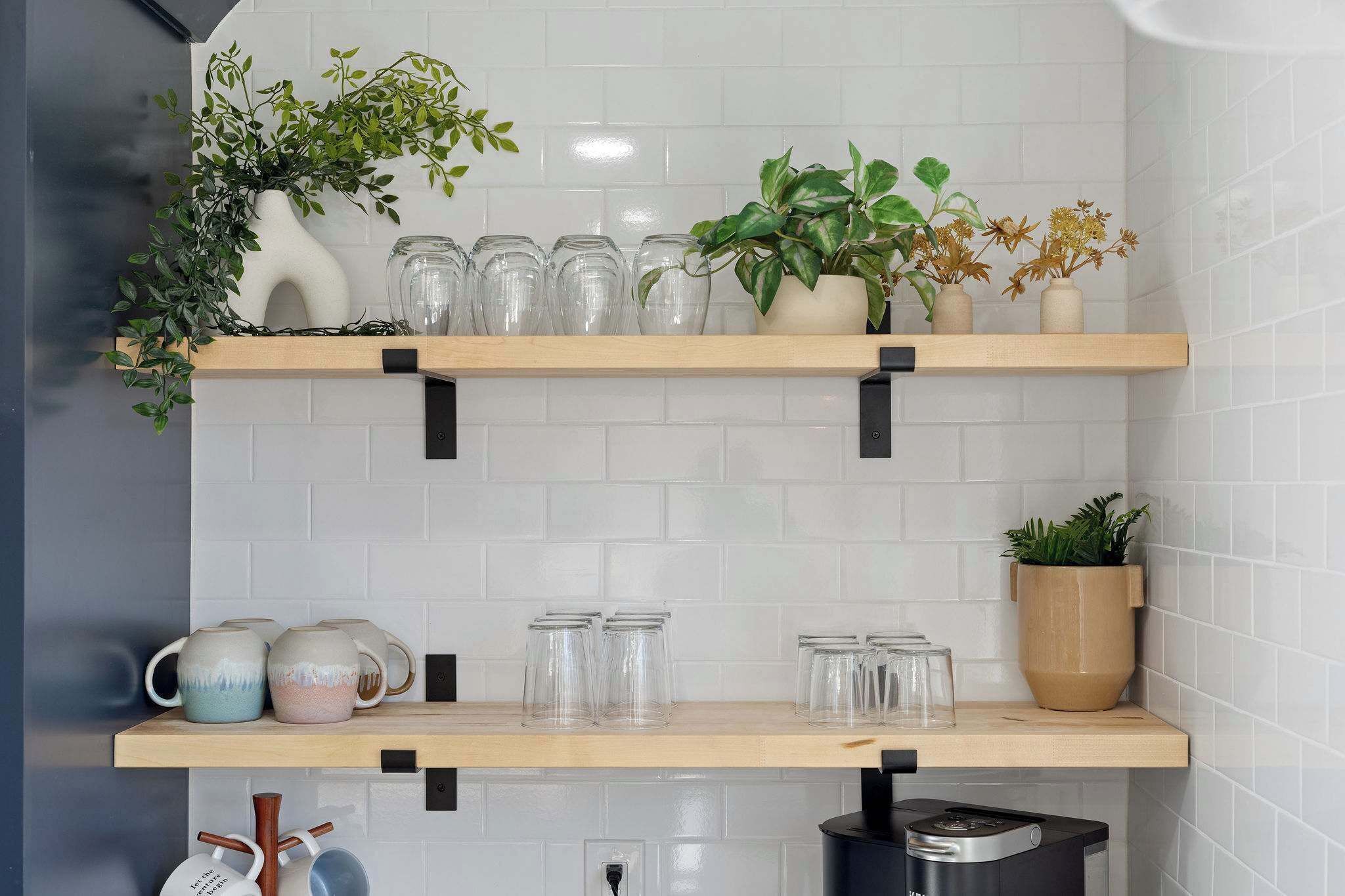 A kitchen with two wooden shelves holding glassware, a plant, and a vase.