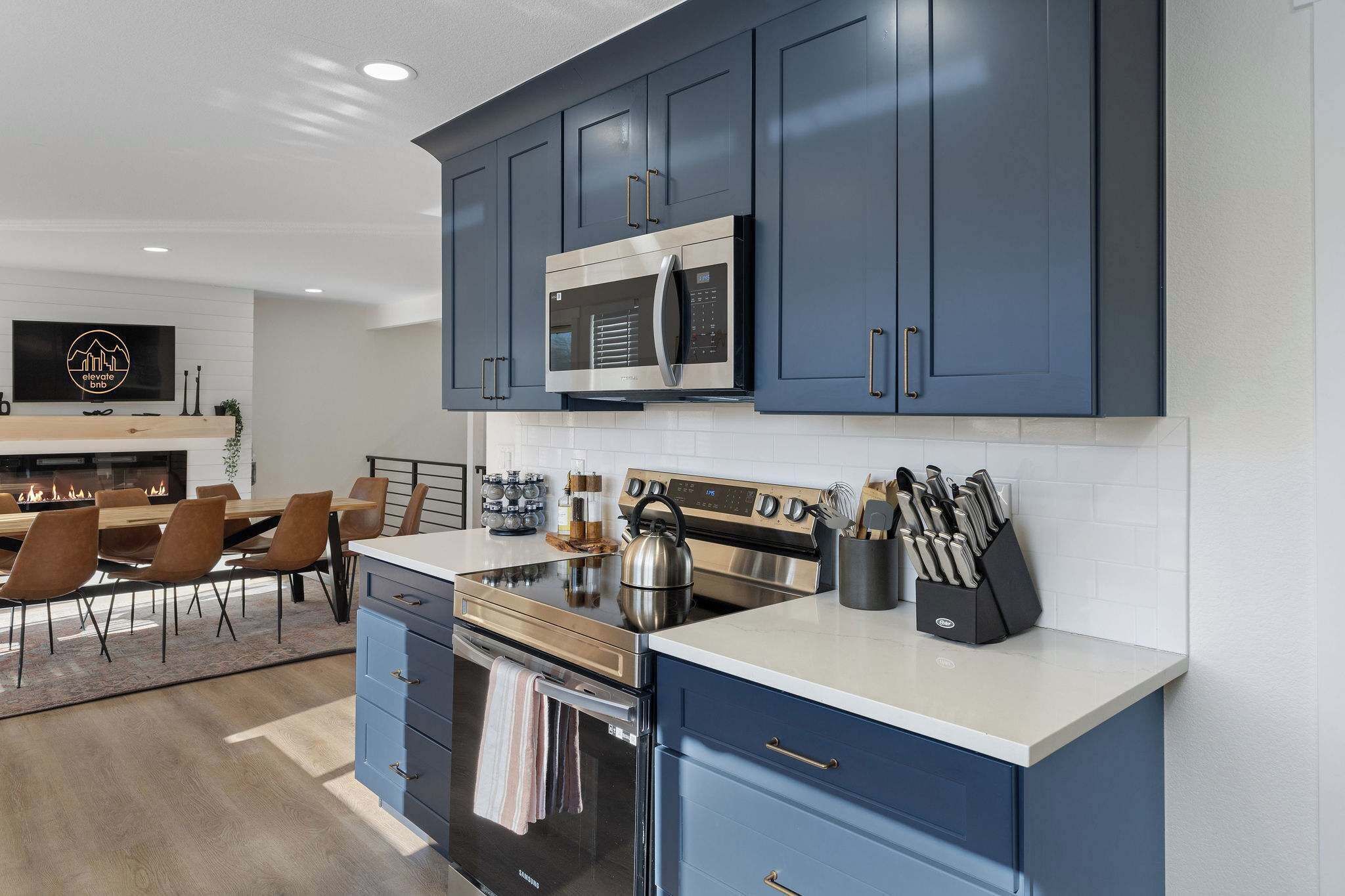 A modern kitchen with dark blue cabinets, stainless steel appliances, and a dining area with a fireplace.