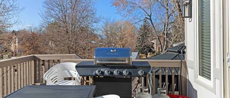 Un barbecue installé sur une terrasse, avec une table et des chaises, une bouteille de gaz et une pelle rouge.