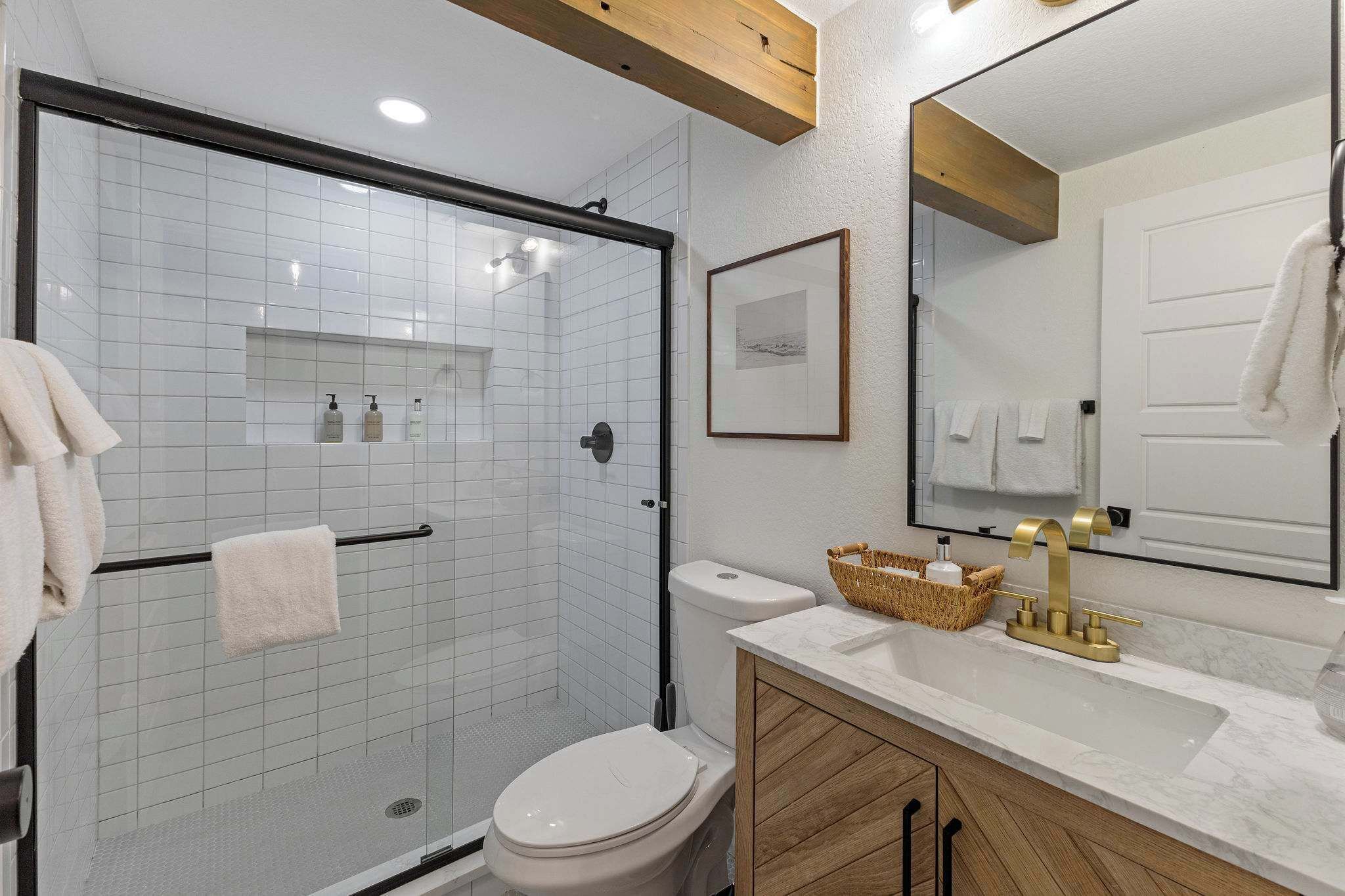 Une salle de bain moderne avec une douche à parois de verre, des toilettes blanches, un meuble-lavabo avec un plan de travail en marbre et un grand miroir.
