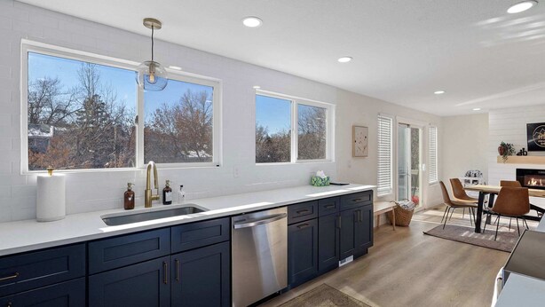 A modern kitchen with dark cabinets, a stainless steel dishwasher, and large windows offering a view of trees and buildings. - Spacious home with Game Room, Hot Tub & Sauna! (Westminster)
