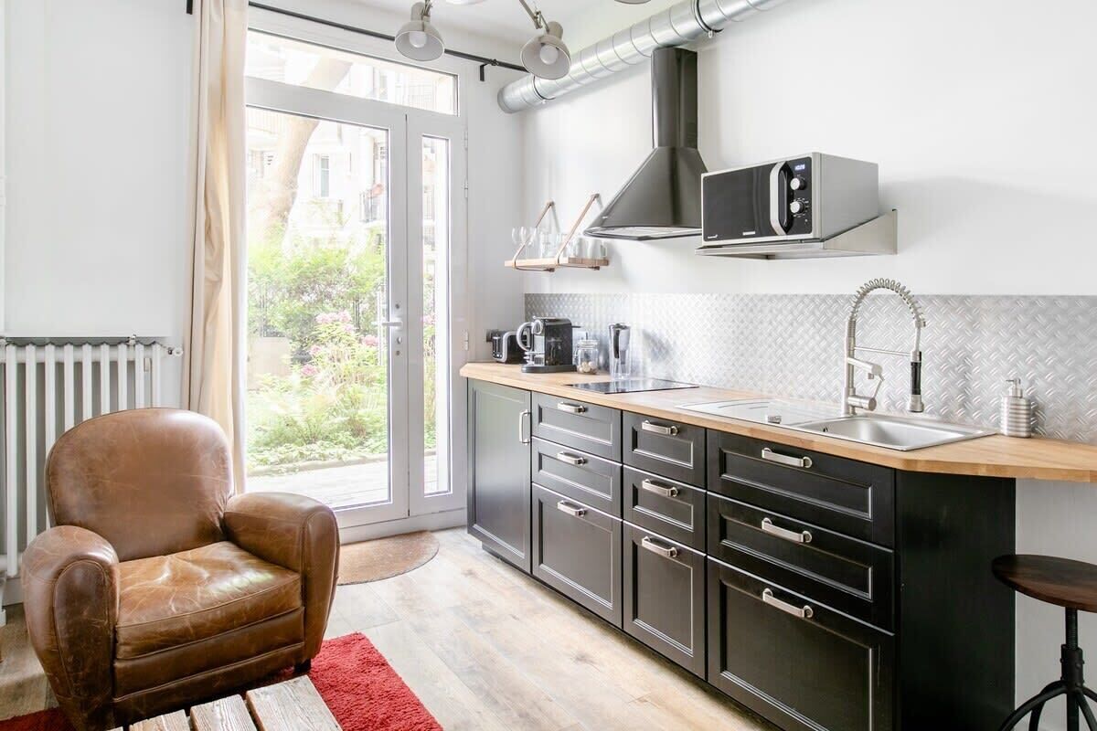 A modern kitchen with a microwave, coffee maker, and a sink. There is a leather chair and a red rug.