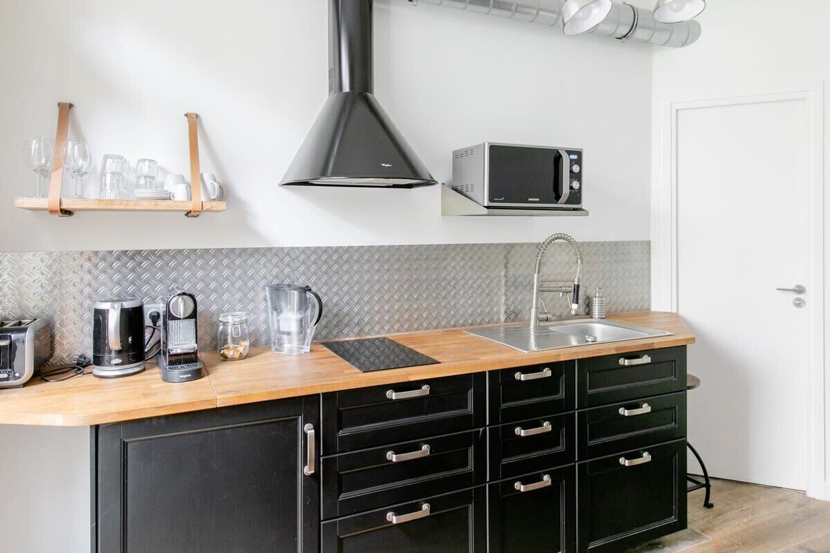 Una cucina con piano di lavoro in legno, pensili neri, lavello in acciaio inossidabile, forno a microonde e cappa aspirante.