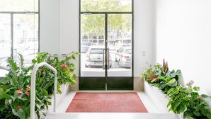 L’entrée d’un hôtel, avec un tapis rouge, une porte en verre et des plantes en pot de chaque côté.