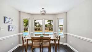 A dining area with a table and chairs, large windows with a view of a backyard and pool, and a ceiling light fixture.