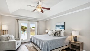A bedroom with a bed, a nightstand, a chair, a ceiling fan, and a window with curtains.