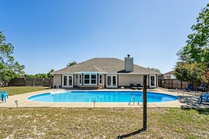 Un jardin arrière d’une maison, avec une piscine, un patio couvert et une cour clôturée.