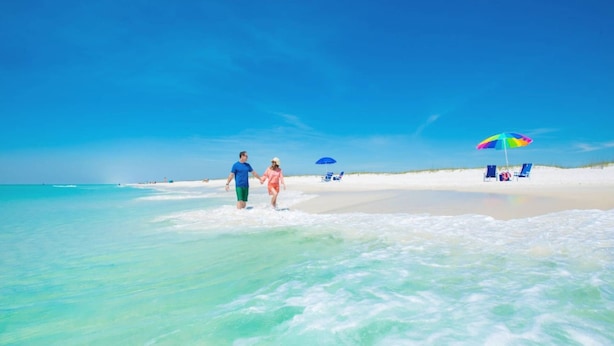 A beach with clear turquoise water, a sandy shore, and a few beach umbrellas.