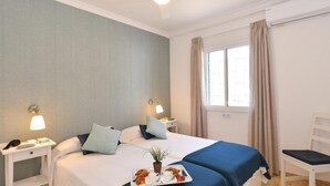 Une chambre d’hôtel avec deux lits, un bureau, une chaise, un ventilateur de plafond et une fenêtre avec des rideaux.
