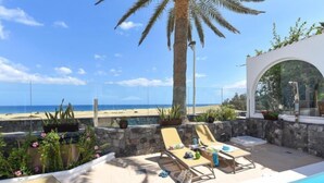 Un espace aménagé au bord de la piscine, avec des chaises longues, un palmier et une vue sur la plage.