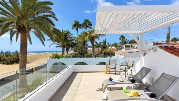Une terrasse sur le toit, dotée de chaises longues, d’une balustrade en verre et offrant une vue sur la plage et les palmiers.