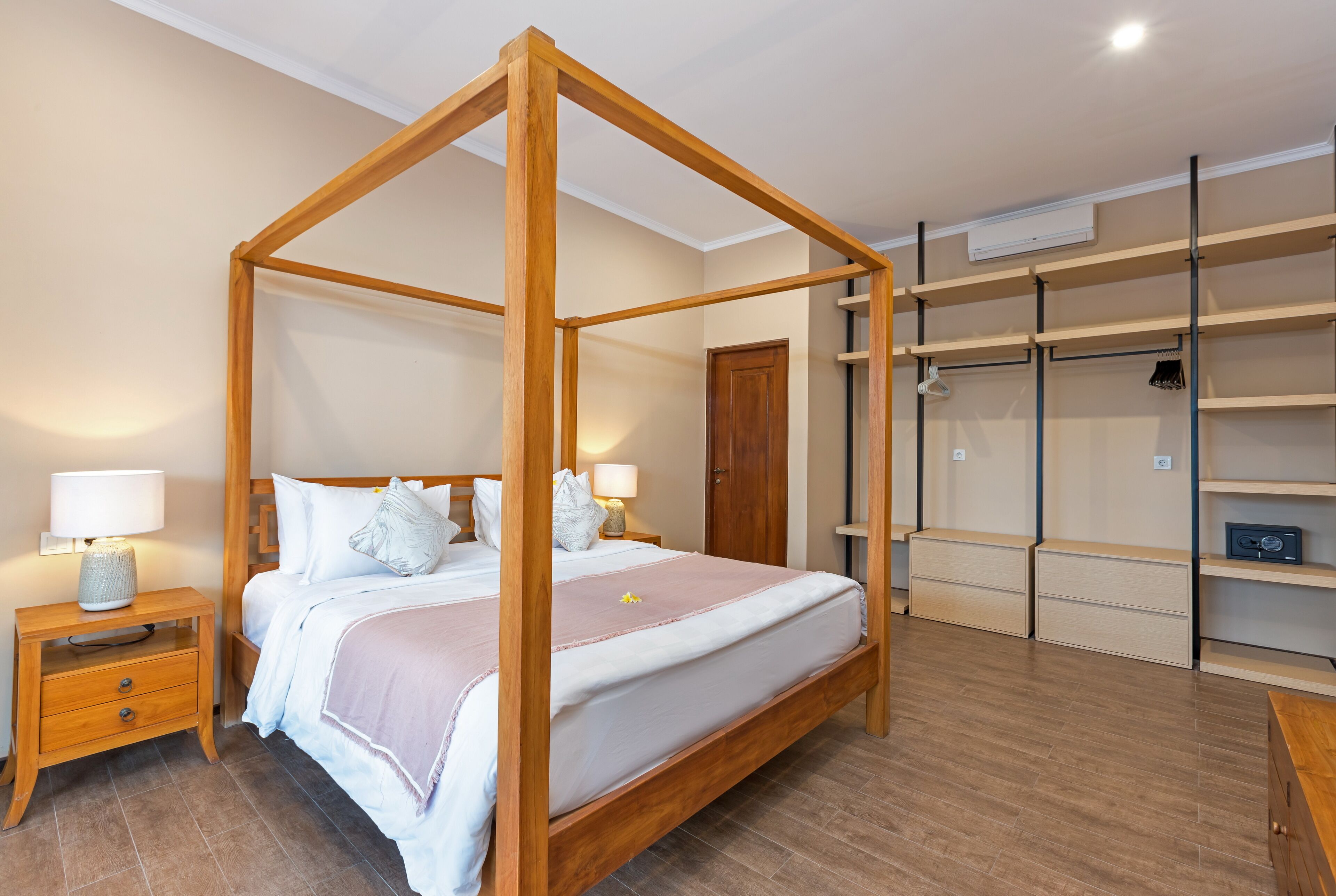 Una camera da letto con un letto a baldacchino, comodini in legno, un tavolino da notte con una lampada, un armadio con scaffali e una porta.