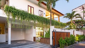 Une maison moderne dotée d’un porche abrité, d’un portail en bois et d’une végétation luxuriante.