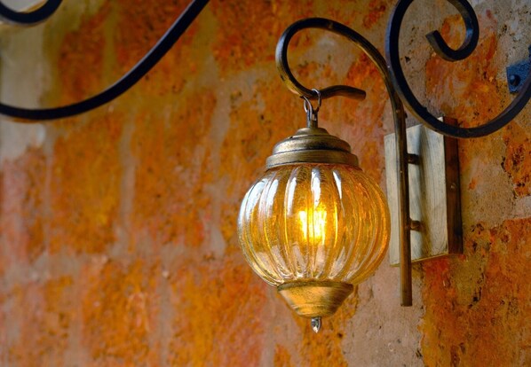 A vintage-style wall-mounted light fixture with a clear glass shade and a metal base, attached to a textured wall with a rustic appearance.