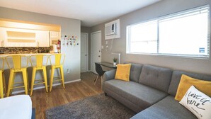 A modern living room with a grey sofa, yellow chairs, a small table, and a large window. - Montrose Relaxing Studio! Medical Center 37 (Houston)