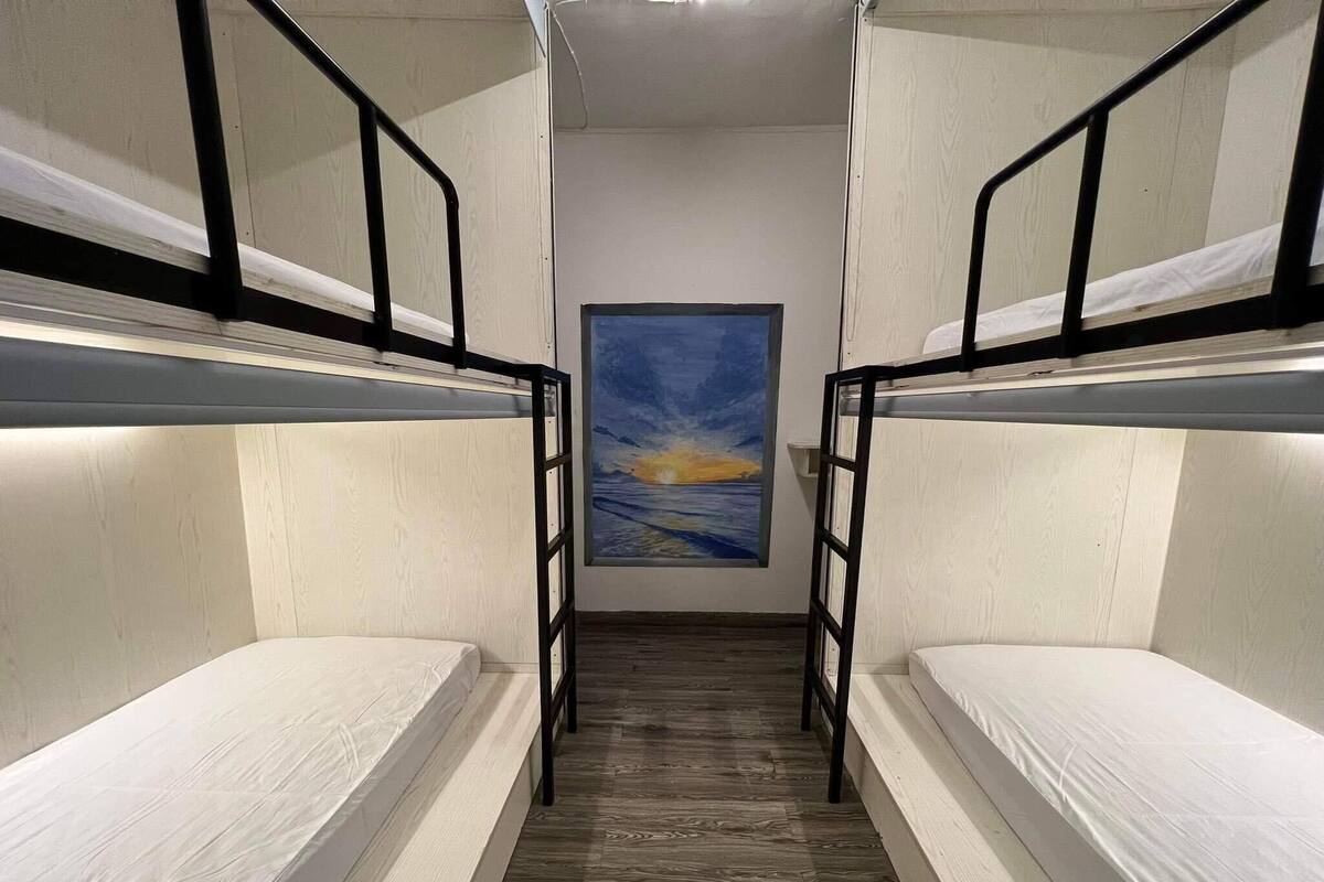A narrow room with bunk beds and a painting of a sunset on the wall.
