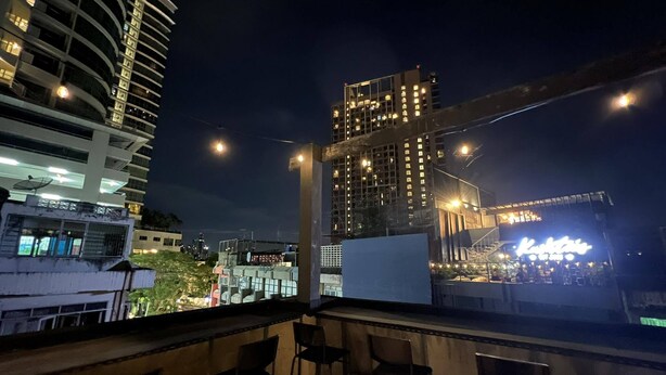 A rooftop terrace with chairs and a view of city buildings at night. - comfy crib hostel  (Bangkok)