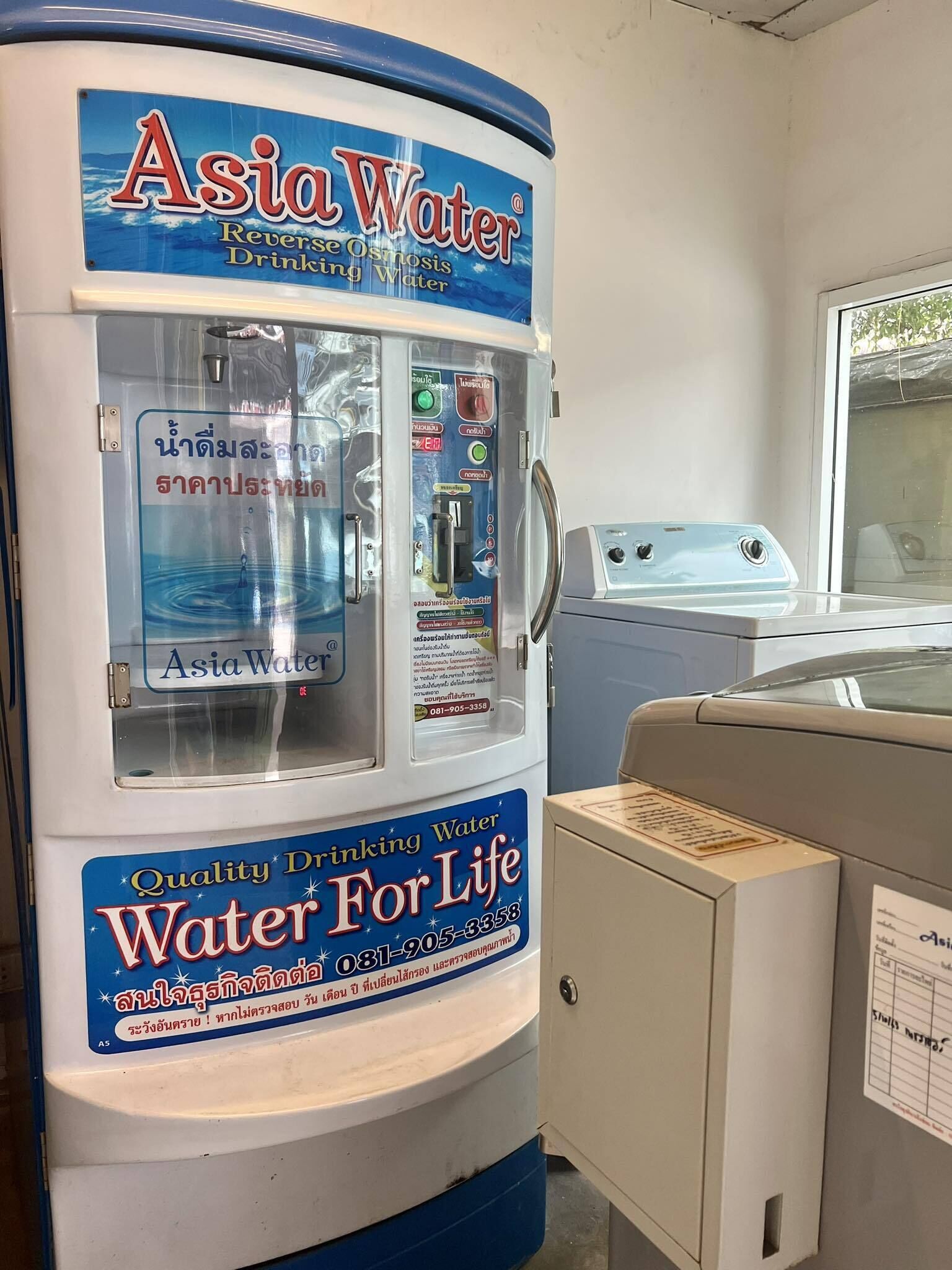Un dispensador de agua etiquetado como "Asia Water" con un cartel que dice "Agua Potable de Calidad Para la Vida" y un número de contacto.