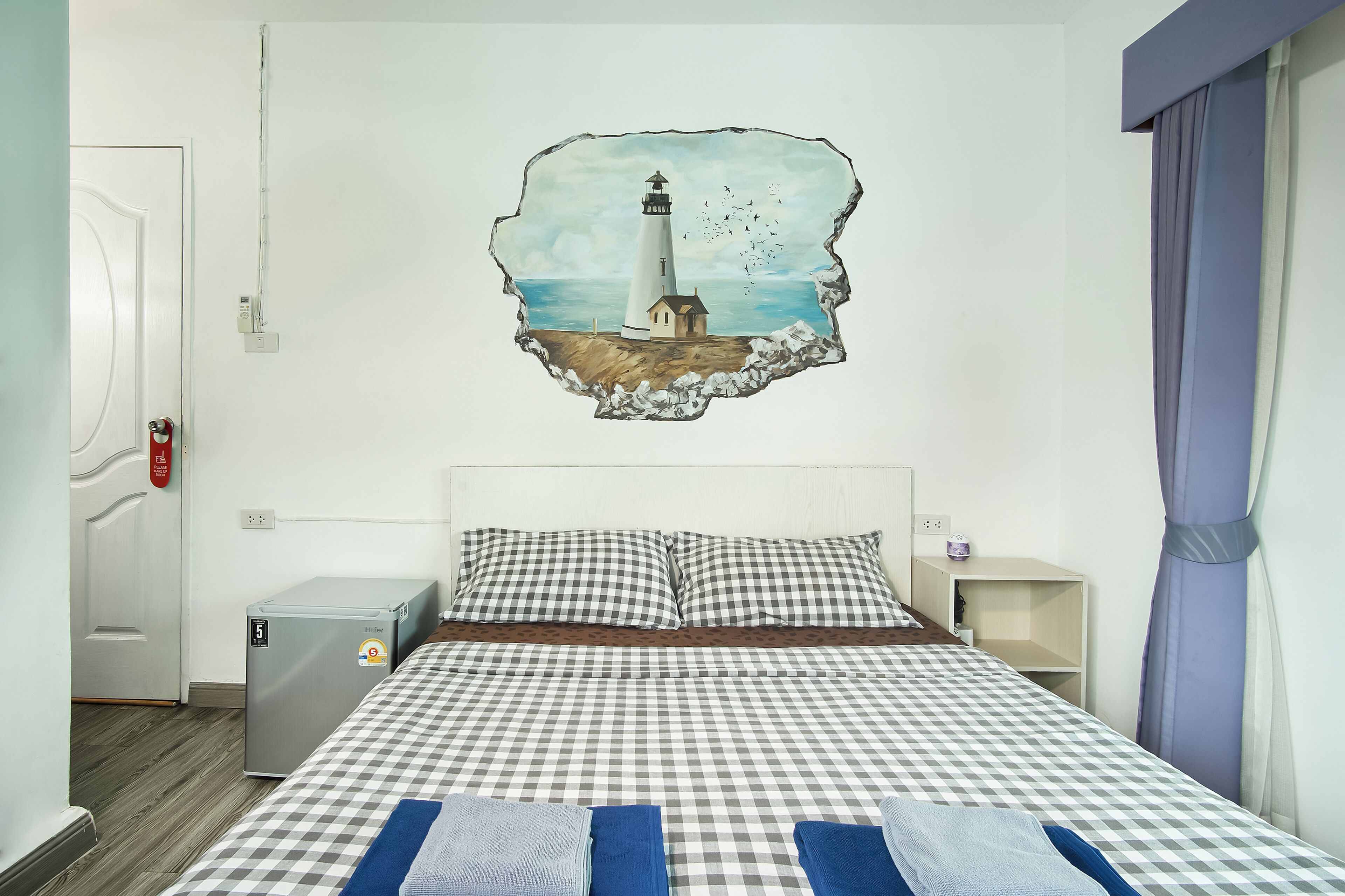 Ein Hotelzimmer mit einem Bett, einem kleinen Nachttisch, einer Wandheizung und einer Wanddekoration mit einem Leuchtturm.